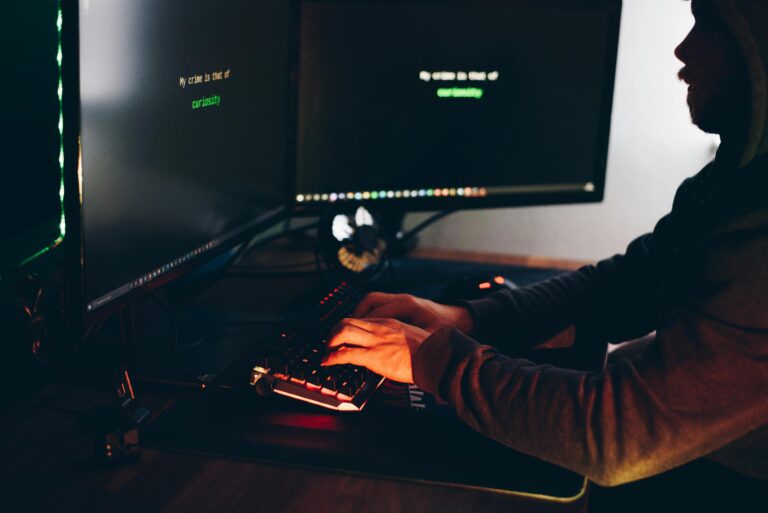 Hacker con capucha frente a pantalla código binario amenaza